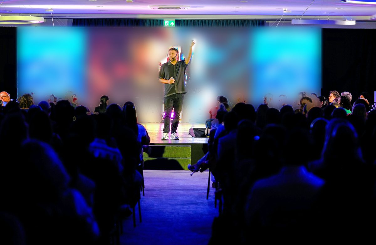 Palestrante no palco falando para a plateia em um evento de tecnologia